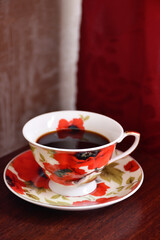 A cup of black coffee on a saucer with poppies.