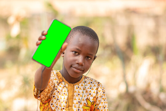 african kid shows the screen of a phone towards the camera, phone has green screen