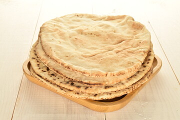 Several freshly baked pita bread on a bamboo plate, close-up, on a wooden table.