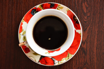 Cup of black coffee on the saucer with red poppies against the background of wooden table. View from above. 