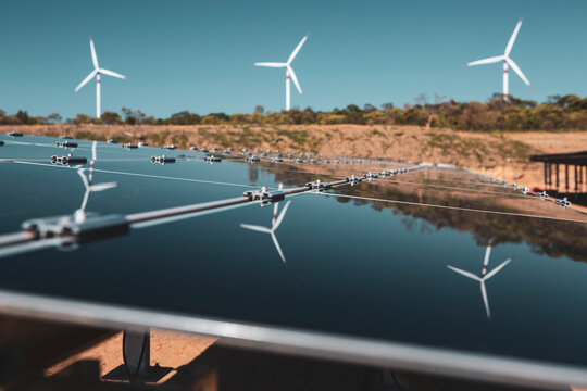 Solar panels under a beautiful blue sky reflecting windmills of an eolic windfarm. Renewable energy generation for environmental conservation concept. 