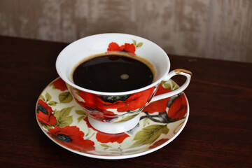 Elegant cup of black coffee on the saucer with red poppies. 