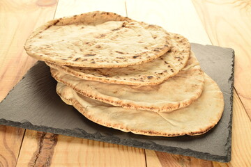 Several freshly baked pita bread on a slate board, close-up, on a wooden table.