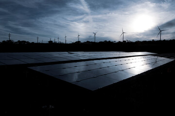 Wind farm and solar panels under a beautiful white sunset among the clouds. Renewable energy generation for environmental conservation concept. 