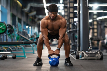Muscular shirtless black man bodybuilder exercising with kettlebell at gym