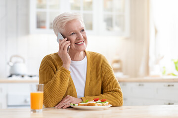 Attractive elderly woman having lunch and talking on phone