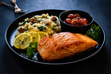 Fried salmon steak with risotto and  tomatoes roasted served on black plate on black wooden table
