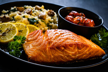 Fried salmon steak with risotto and  tomatoes roasted served on black plate on black wooden table
