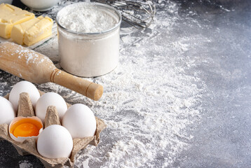 Baking ingredients: flour, eggs, butter and sugar, with rolling pin on a table