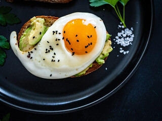Continental breakfast - sunny side up eggs on toasted bread with avocado on black background
