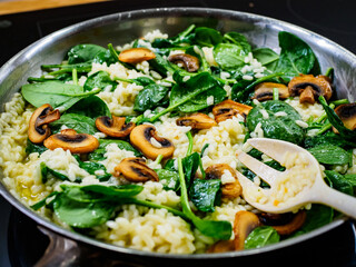 Risotto with champignons and spinach cooking in frying pan
