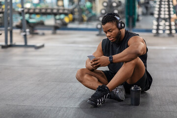Tired black guy bodybuilder sitting on floor, listening to music
