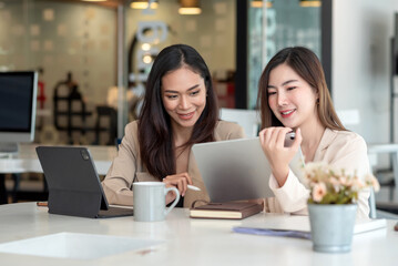 Two young asian woman discuss concept work at the office using a tablet.