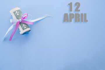 calendar date on blue background with rolled up dollar bills pinned by blue and pink ribbon with copy space. April 12 is the twelfth day of the month