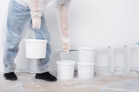 a worker in a disposable white overalls brought buckets of paint to renovate the premises