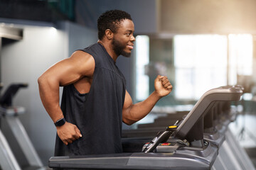 Fototapeta na wymiar Motivated african american guy in black sportswear jogging at gym