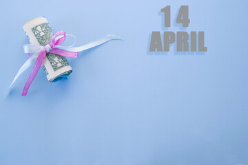 calendar date on blue background with rolled up dollar bills pinned by blue and pink ribbon with copy space. April 14 is the fourteenth  day of the month