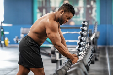 Fototapeta na wymiar Shirtless african american bodybuilder grabbing dumbbell in gym