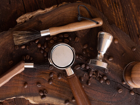 Barista coffee tools (tamper, distribution leveling tool, brushes) and roasted coffee beans on wooden board