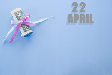 calendar date on blue background with rolled up dollar bills pinned by blue and pink ribbon with copy space. April 22 is the twenty-second day of the month