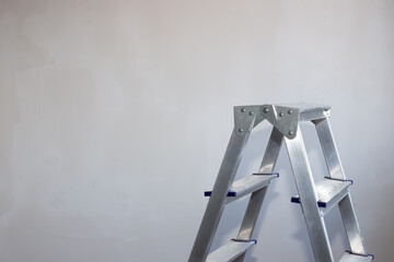 an aluminum stepladder stands against a gray wall. Repair and improvement of housing. Copy space to the left.