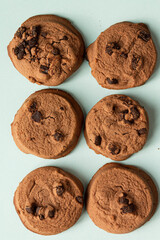 Chocolate cookies with chocolate pieces are creatively arranged on a turquoise background. Space for text