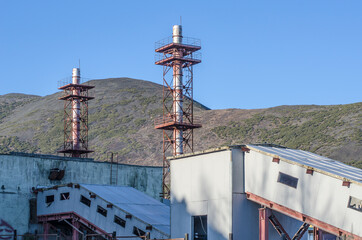 Fragment of factory buildings with pipes against the background of the mountains.