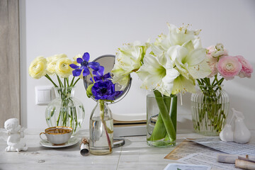 A bouquet of white roses in a round glass vase, a bouquet of white amaryllis, a cup of tea, a figurine on the table. Decoration of the kitchen. Rose Playa blanca
