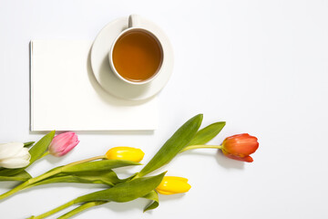 Multicolored tulips near a white blank notebook and cup of tea