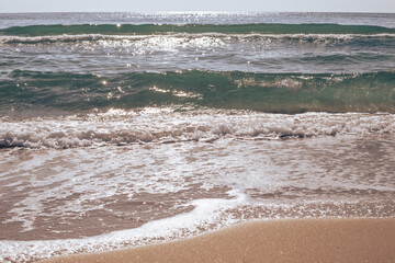 Sunny day at the seaside. A wave runs onto the sandy shore, sparkling in the sun. Warm pleasant colors. Travel and tourism.
