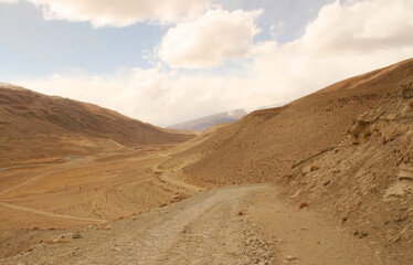 Fototapeta na wymiar Pamir Highway in the desert landscape of the Pamir Mountains in Tajikistan. Afghanistan is on the left