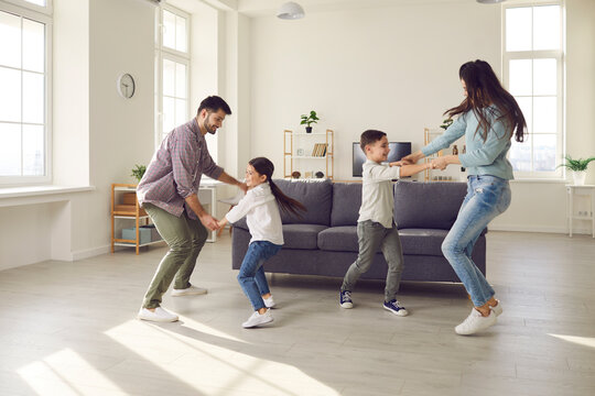Happy family spending quality time at home. Couple with children playing, dancing and having fun in big new room. Little boy, girl and parents enjoying leisure in Covid19 coronavirus lockdown together