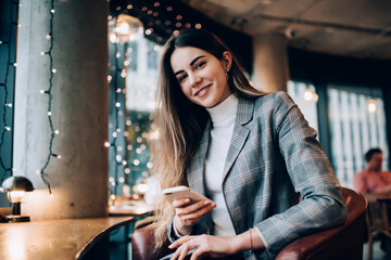 Happy female using smartphone for chatting in cafeteria