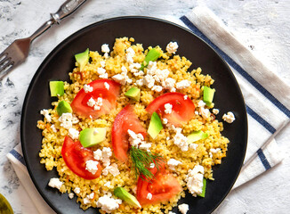 Bulgur with vegetables on a plate. Black background. Top view