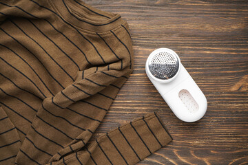 Modern fabric shaver and clothes on wooden background. Flat lay.