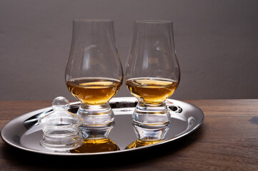 Tasting glasses of single malt scotch whisky served on steel mirror tray with reflection