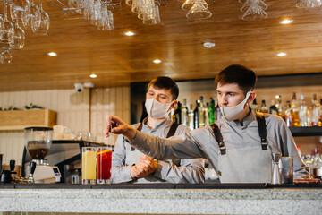Two stylish bartenders in masks and uniforms during the pandemic, preparing cocktails. The work of restaurants and cafes during the pandemic.