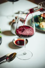Rolgordijnen Selective focus shot of pouring red wine into the glass on a white table, dinner table at restaurant © Aleksandrs Muiznieks