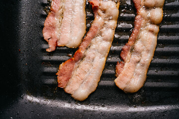 Close-up Top view of frying sizzling bacon strips in a pan with hot greasing bacon oil for making crispy bacon. Keto snack meal.
