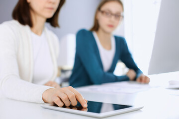 Obraz premium Businesswoman pointing at tablet computer screen while giving presentation to her female colleague. Group of business people working at the desk in office. Teamwork concept