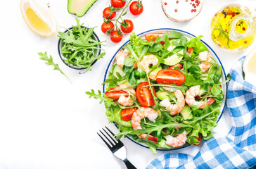 Fresh shrimp salad with tomatoes, lettuce, arugula, avocado, cucumber and lemon dressing on white background. Healthy eating, clean food concept. Top view