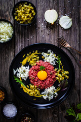 Beef tartare steak with onion, capers and pickled cucumbers on wooden table