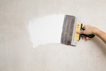 Young adult man hand using spatula and plastering wall with white fresh finishing putty. Closeup....