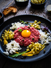 Beef tartare steak with onion, capers and pickled cucumbers on wooden table
