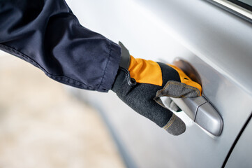 Male auto mechanic hand wearing protective glove holding car door handle in auto service garage. Mechanical maintenance engineer working in automotive industry. Automobile servicing and repair