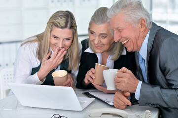 three mature businesspeople using laptop and drinking coffee