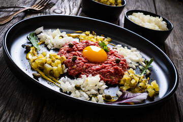 Beef tartare steak with onion, capers and pickled cucumbers on wooden table