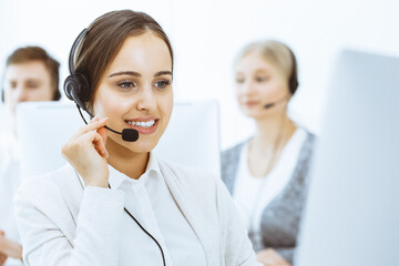 Call center. Group of diverse operators at work. Beautiful woman in headset communicating with customers of telemarketing service. Business concept - obrazy, fototapety, plakaty
