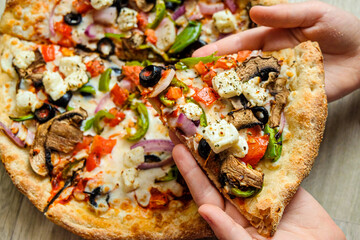 Children's hands hold a slice of pizza. Wooden background. Top view