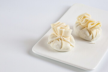 Georgian traditional Khinkali with Suluguni cheese, nuts, greens, spices. Khinkali lie on a flat white plate. Copy space. White background.